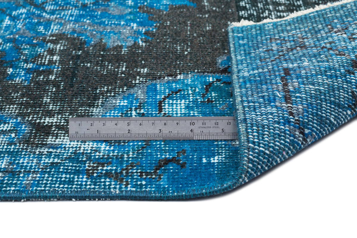 Blue and charcoal distressed abstract rug with a folded corner and a metal ruler for scale on a white background.