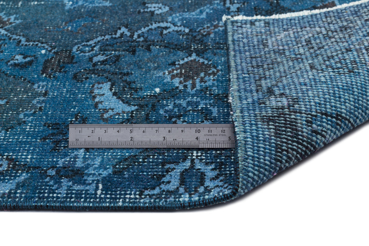 Blue and black distressed floral pattern rug with a corner folded back to show the woven backing and a metal ruler.