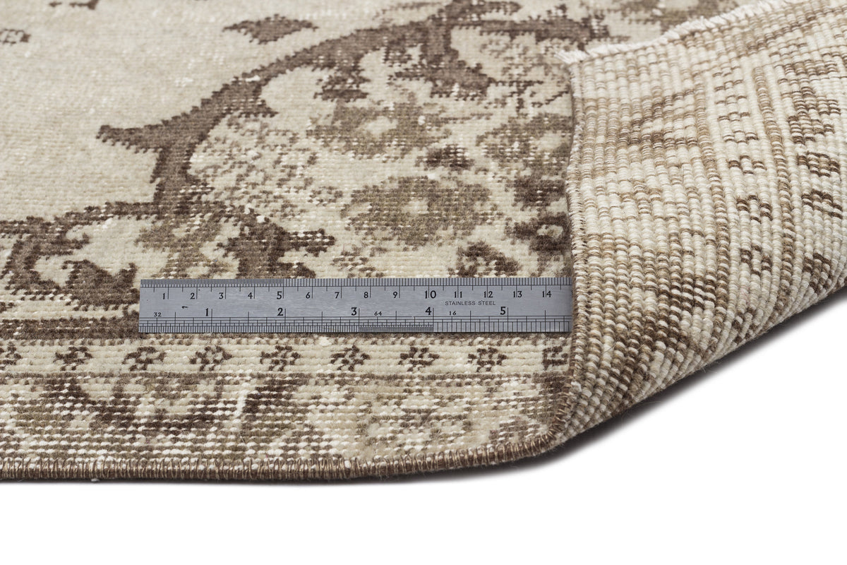 Beige and brown distressed medallion rug with a folded corner and a metal ruler for scale on a white background.