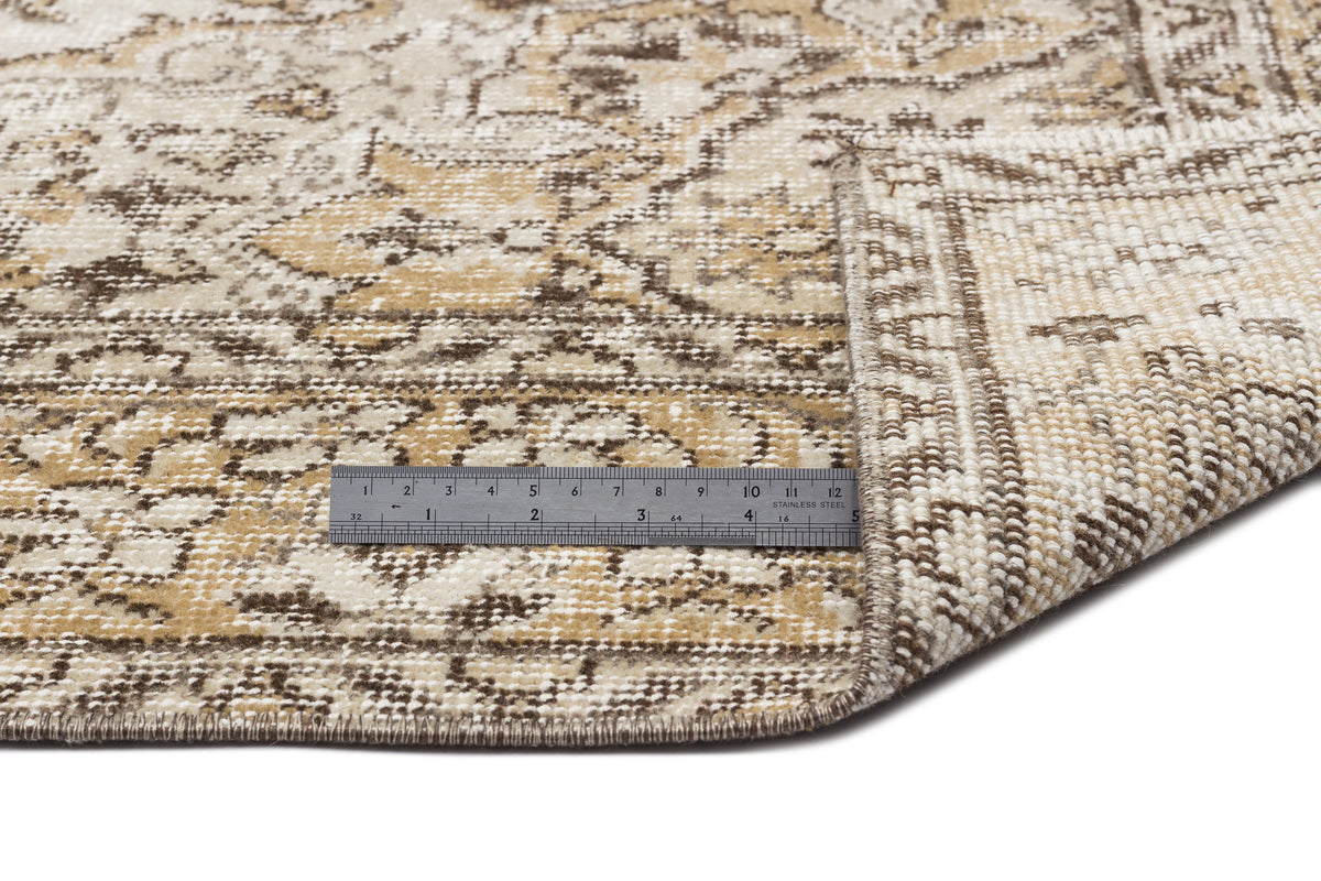 Tan and brown distressed medallion rug with a folded corner and a metal ruler for scale on a white background.