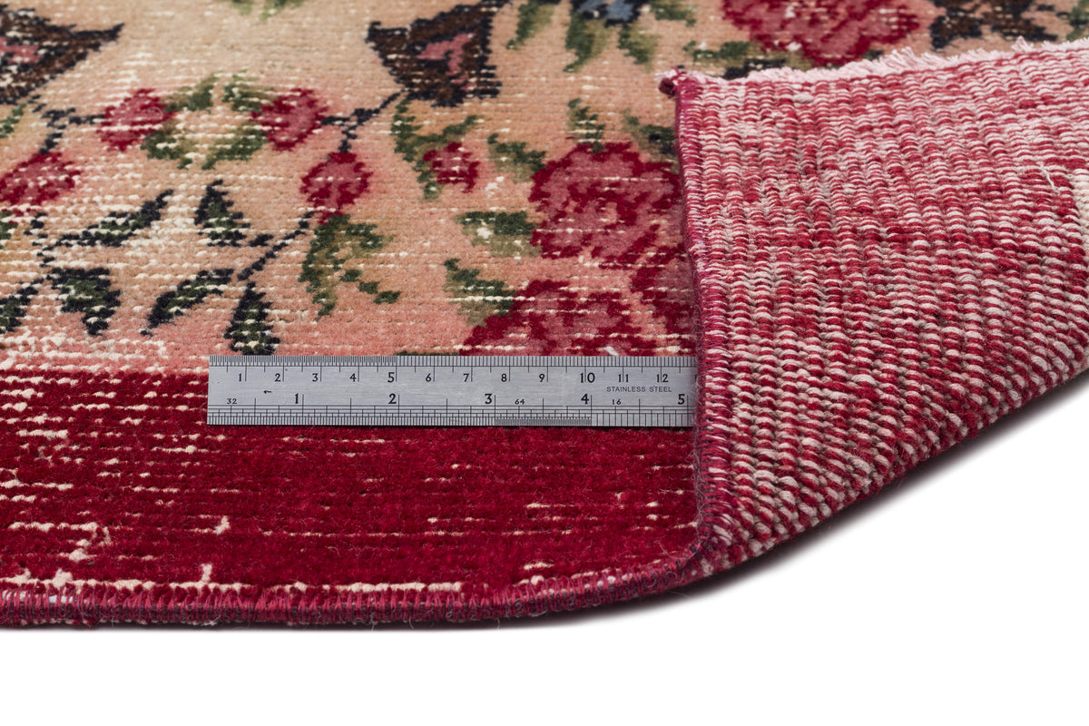Floral rug with a pink and red distressed pattern, showing the woven backing and a metal ruler for scale.