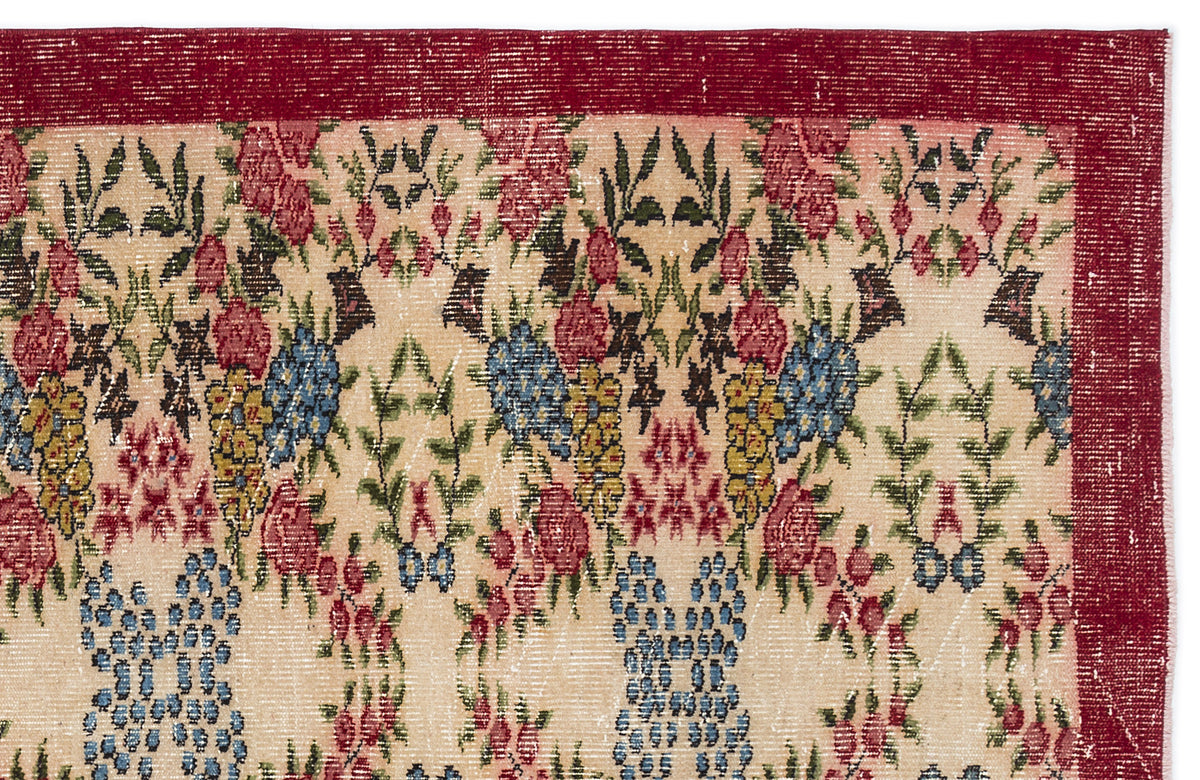 Beige rug with a red border and a repeating floral pattern in red, blue, yellow, and green on a white background.