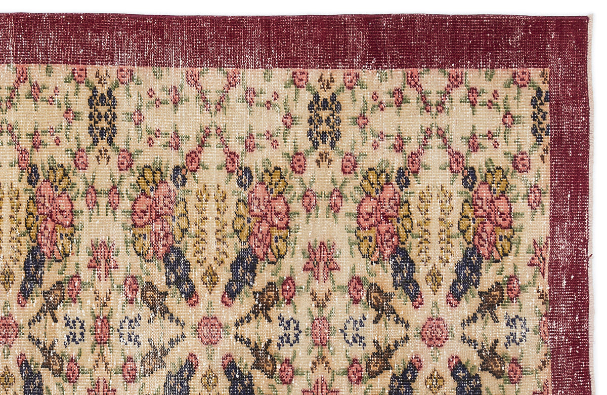 Beige rug with a distressed floral pattern in red, yellow, and navy, featuring a wide solid dark red border.