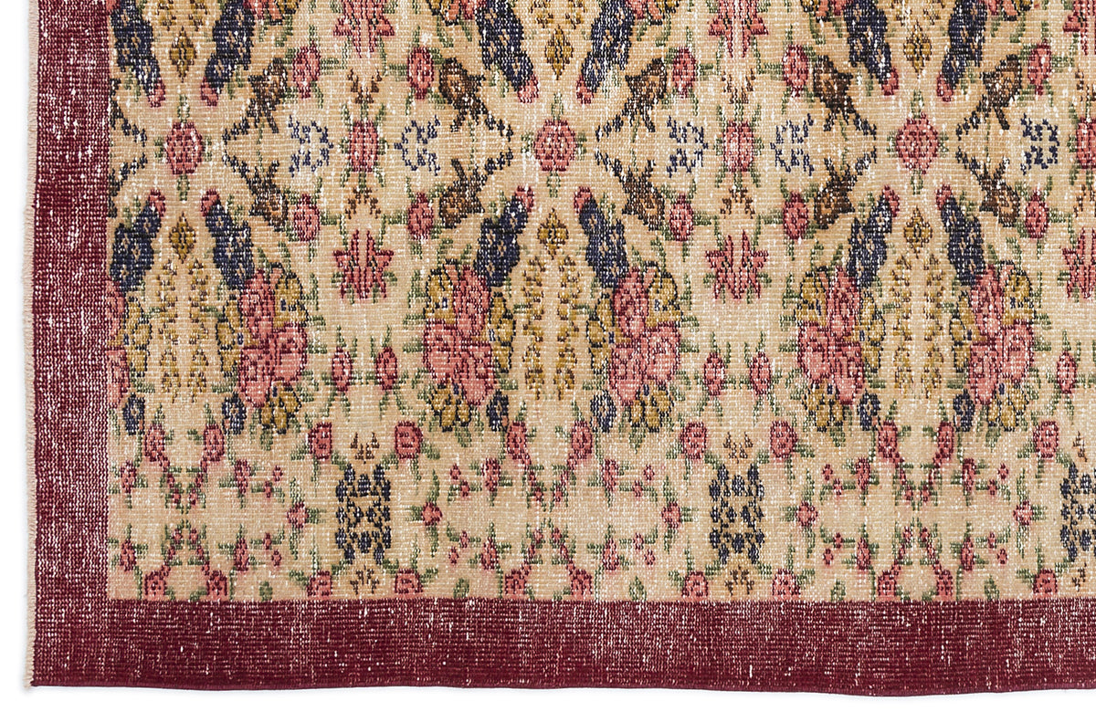 Beige rug with a distressed floral medallion pattern in pink, navy, and green, featuring a solid deep red border.