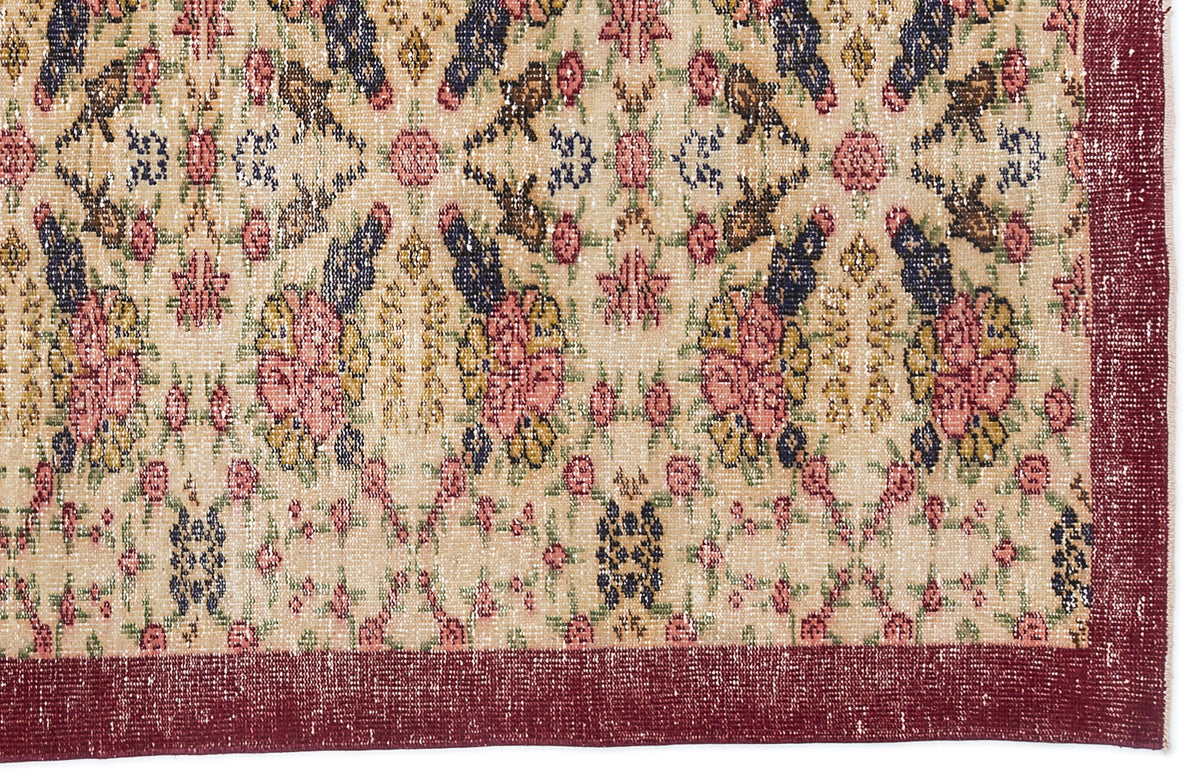 Beige rug with a distressed floral medallion pattern in pink, navy, and mustard, featuring a solid dark red border.