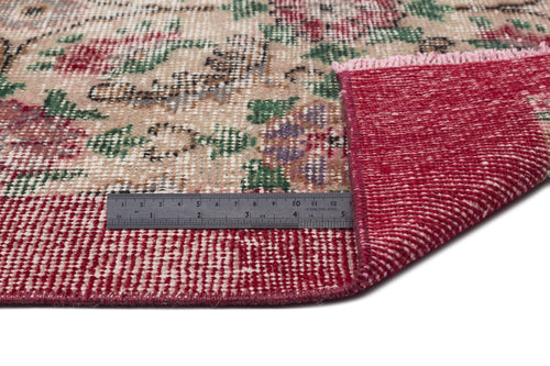 Load image 1 in gallery view. Beige rug with a distressed floral pattern in red, green, and purple, showing a folded corner and a metal ruler.