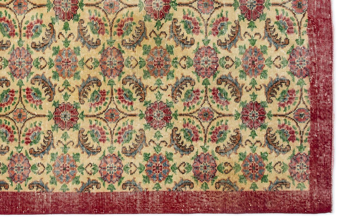 Beige rug with a repeating floral medallion pattern in red, green, and blue, featuring a wide red border.