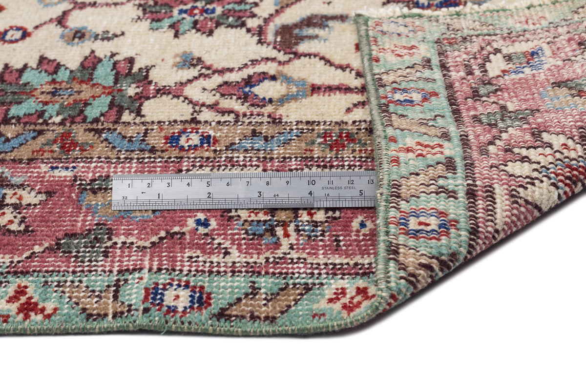 Vintage-style rug with a floral medallion pattern in cream, red, and teal, shown with a metal ruler for scale.
