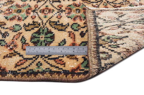Load image 1 in gallery view. Tan, green, and rust floral patterned rug with a folded corner and a metal ruler for scale on a white background.