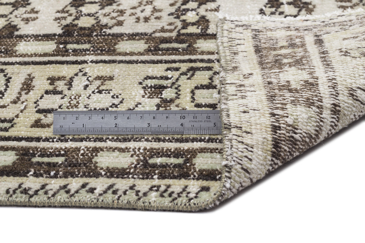 Beige and brown distressed rug with a geometric border pattern, shown with a metal ruler for scale.