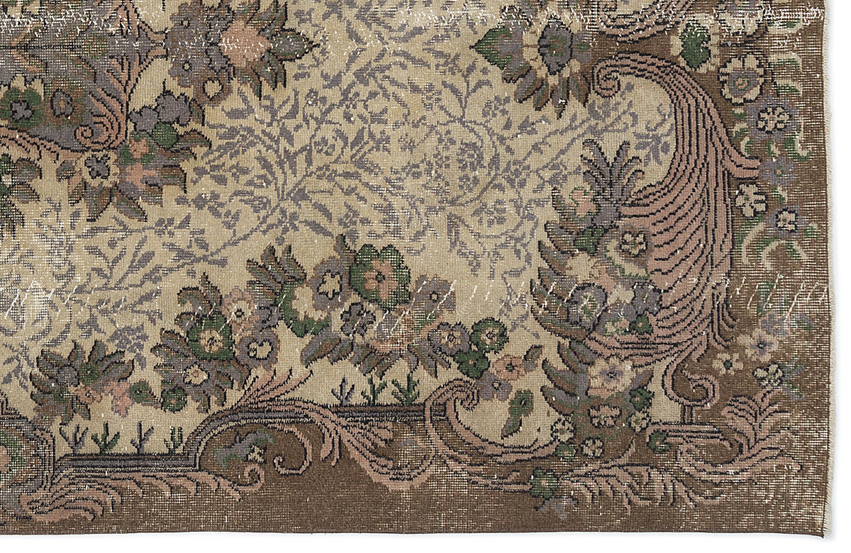 Distressed beige rug with a brown border and intricate floral, vine, and paisley patterns in muted green, grey, and pink.