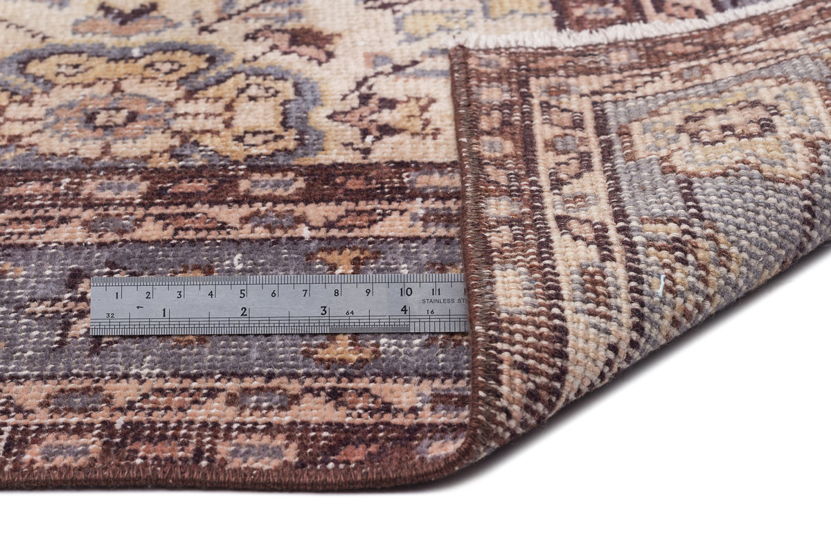 Brown, beige, and grey traditional patterned rug with a folded corner and a metal ruler for scale on a white background.