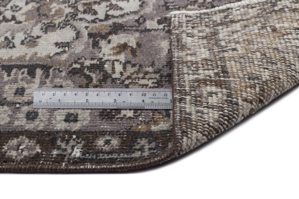 Grey and brown distressed traditional rug with a folded corner and a metal ruler for scale on a white background.