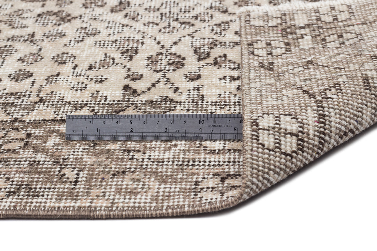 Beige and brown distressed floral rug with a corner folded over, showing the woven backing and a metal ruler for scale.