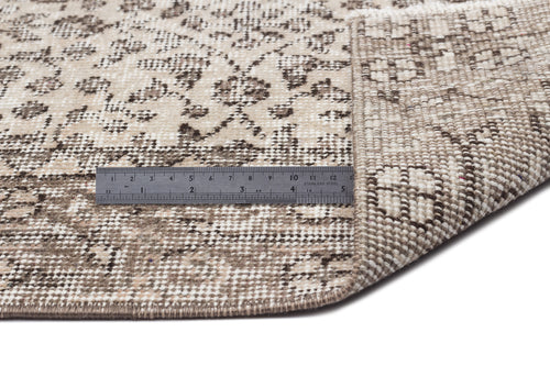 Load image 1 in gallery view. Beige and brown distressed floral rug with a corner folded over, showing the woven backing and a metal ruler for scale.
