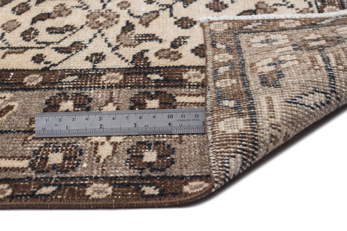 Load image 1 in gallery view. Beige and brown floral patterned rug with a folded corner and a metal ruler for scale on a white background.
