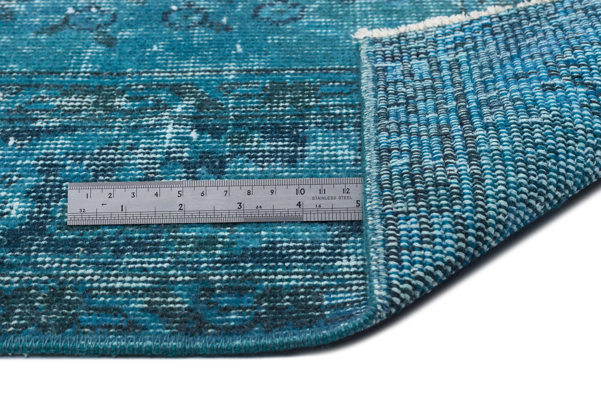 Teal and navy distressed patterned rug with a folded corner and a metal ruler for scale.
