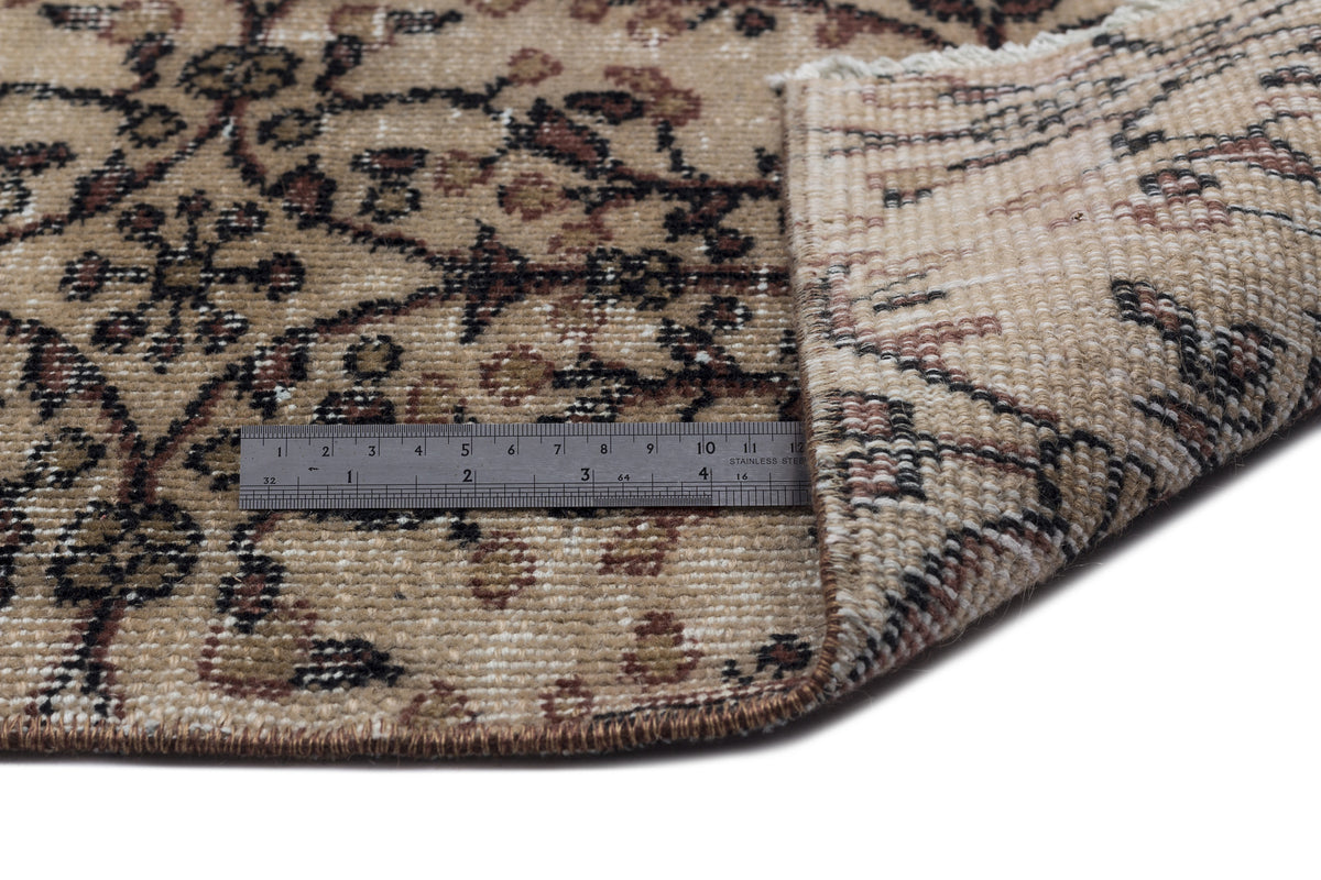 Tan and brown traditional floral rug with a metal ruler showing pile height, isolated on a white background.