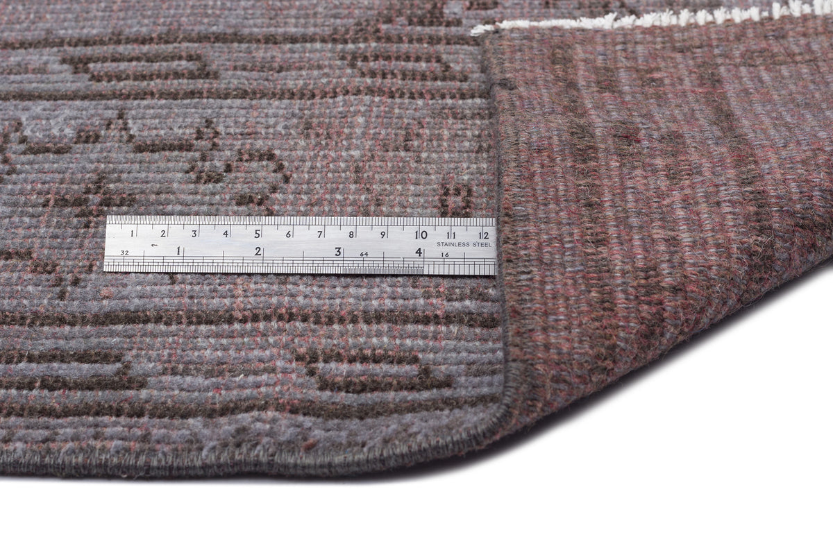 Grey and brown hand-knotted rug with a geometric pattern, shown folded with a stainless steel ruler for scale.