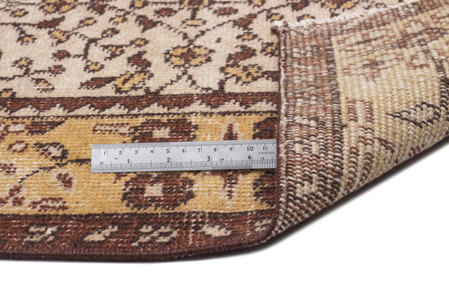 Load image 1 in gallery view. Beige and brown floral patterned rug with a folded corner and a metal ruler for scale on a white background.