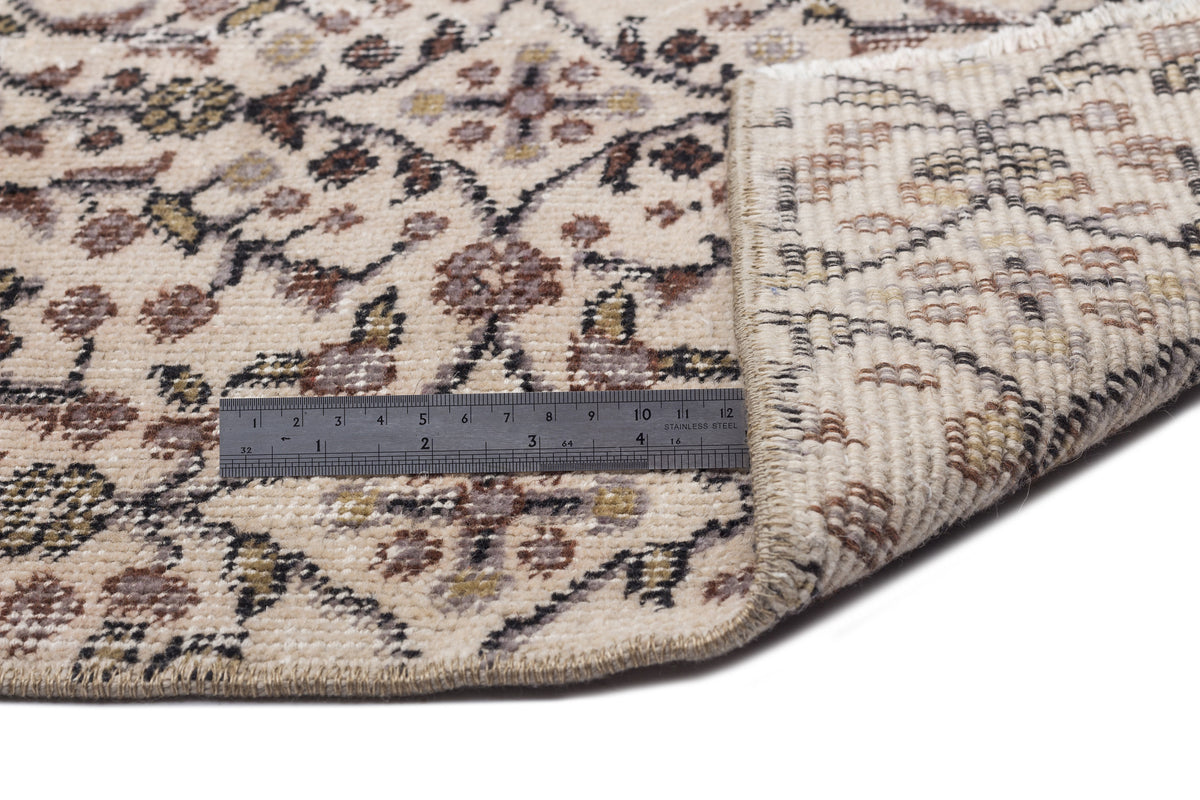 Beige rug with a brown and black floral pattern, shown with a metal ruler for scale and a folded corner.
