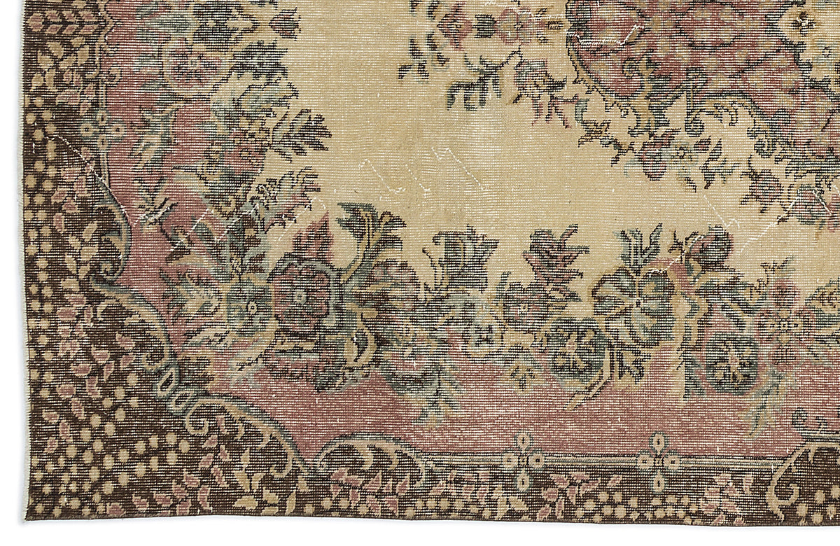 Distressed beige rug with a dark brown border and a faded floral medallion pattern in muted pink, green, and charcoal.