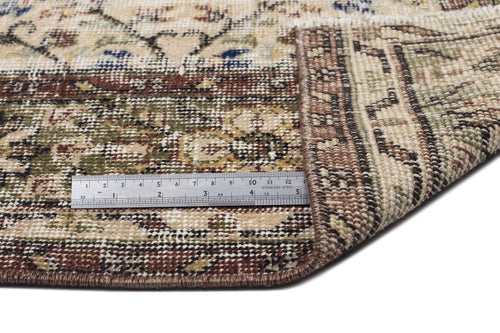 Load image 1 in gallery view. Beige, brown, and olive green traditional floral rug with a folded corner and a metal ruler for scale.
