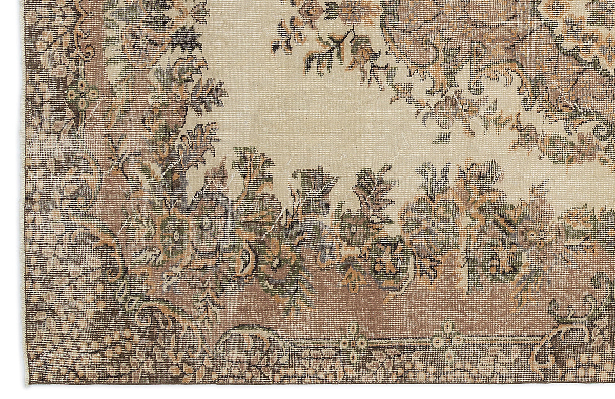 Beige rug with a distressed floral medallion pattern in muted brown, olive green, and charcoal tones.