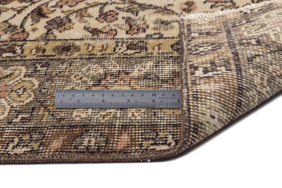 Beige and brown traditional floral rug with a folded corner revealing the weave, shown with a metal ruler for scale.