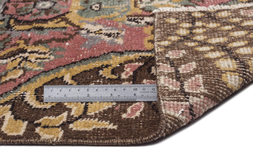 Load image 1 in gallery view. Distressed floral medallion rug in brown, pink, and green with a metal ruler showing pile height on a white background.