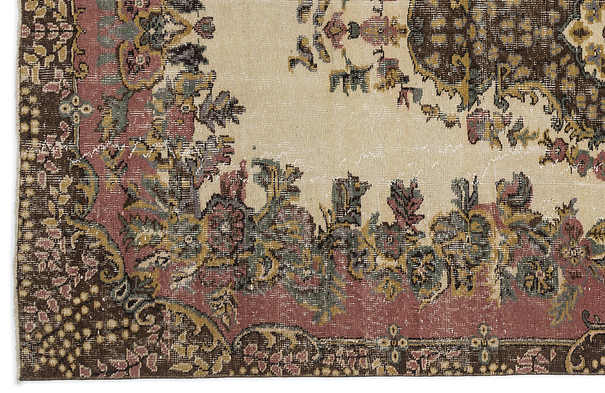 Distressed vintage-style rug with a cream field, dark brown borders, and floral medallion motifs in muted pink and green.