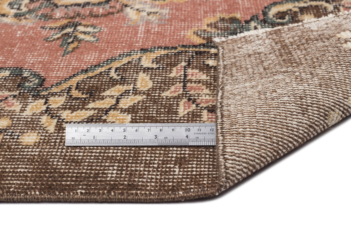 Distressed terracotta and brown rug with a floral medallion pattern, shown with a metal ruler for scale.