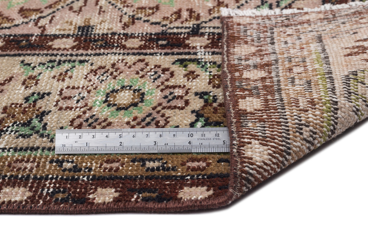 Beige, brown, and green traditional floral medallion rug with a folded corner and a metal ruler for scale.