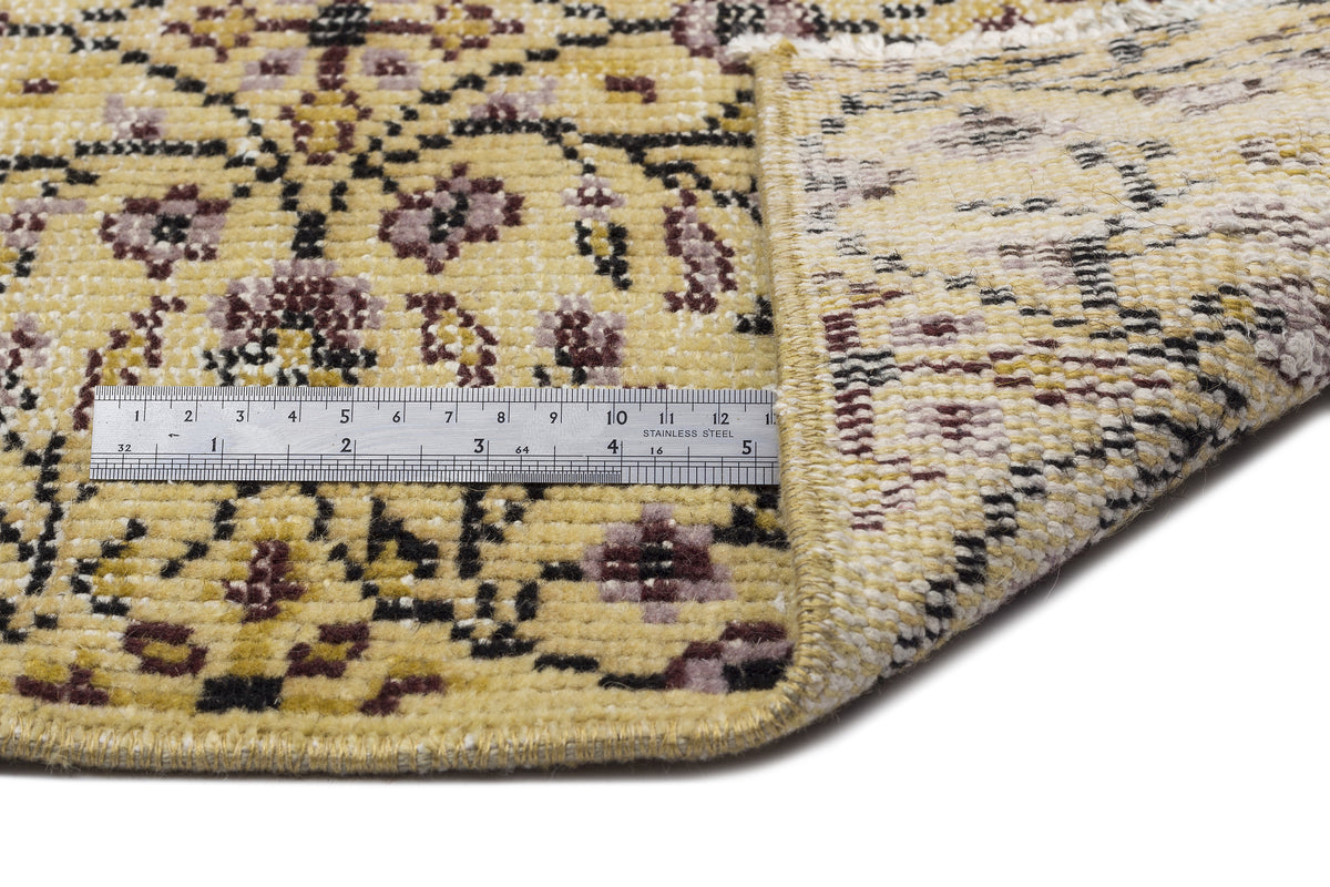 Yellow, black, and mauve floral patterned rug with a folded corner and a metal ruler for scale.