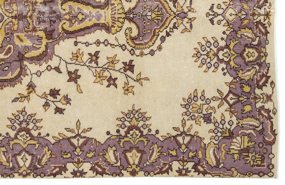 Beige rug with a distressed floral and paisley pattern in muted purple, brown, and mustard yellow.