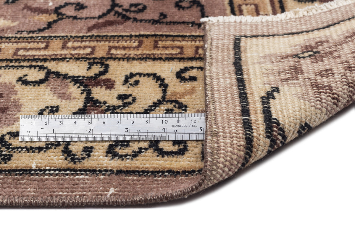 Brown and beige traditional rug with a black floral border, shown with a metal ruler for scale on a white background.