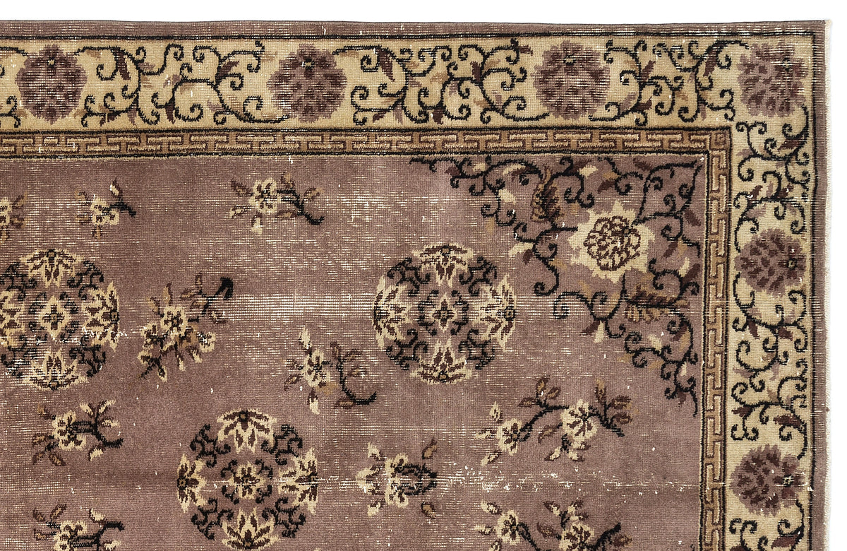 Mauve and beige rug with a distressed floral medallion pattern and a Greek key border.