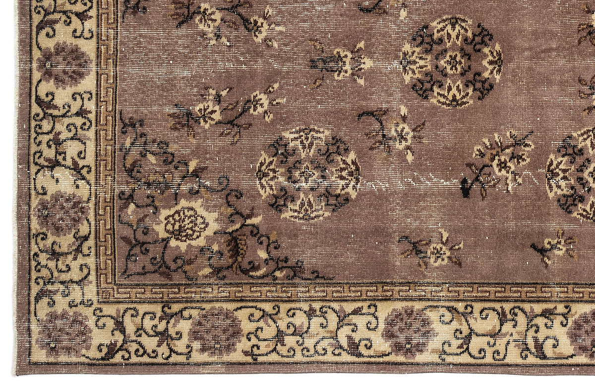 Mauve and beige distressed rug with a traditional floral medallion pattern and a geometric Greek key border.