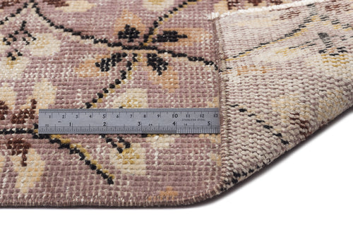 Load image 1 in gallery view. Mauve, cream, and black floral patterned rug with a folded corner and a metal ruler for scale on a white background.
