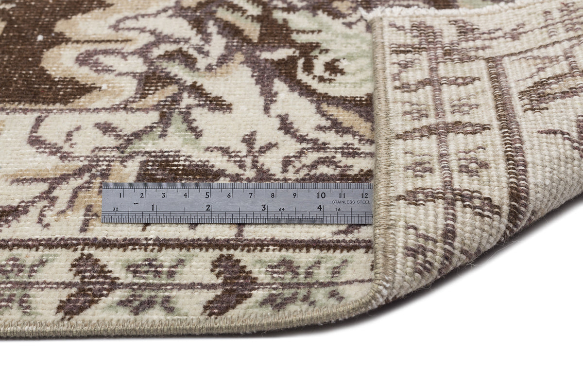 Brown, cream, and sage green traditional floral rug with a folded corner and a metal ruler for scale.