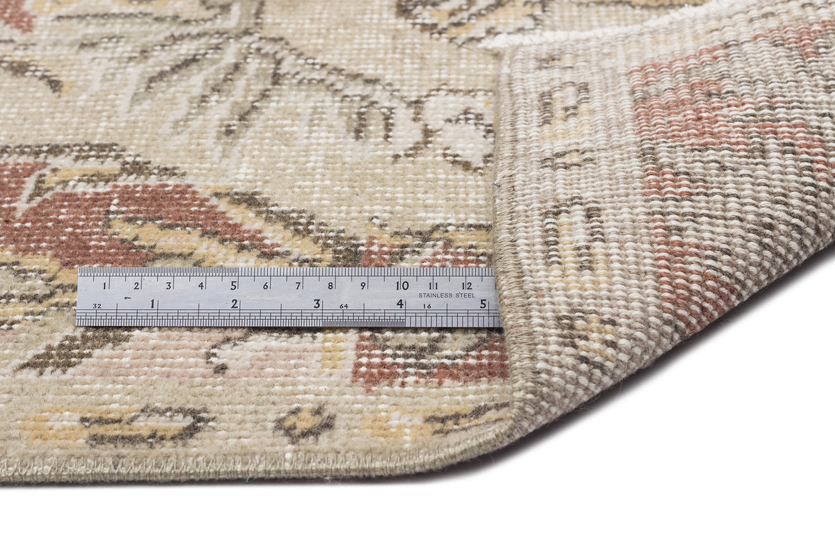 Beige, rust, and brown vintage-style rug with a floral pattern, shown with a metal ruler for scale.