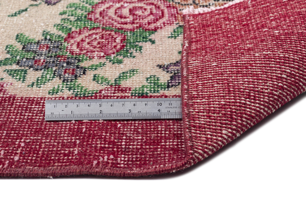 Cream rug with red floral pattern and a folded corner showing the red woven backing, measured by a metal ruler.