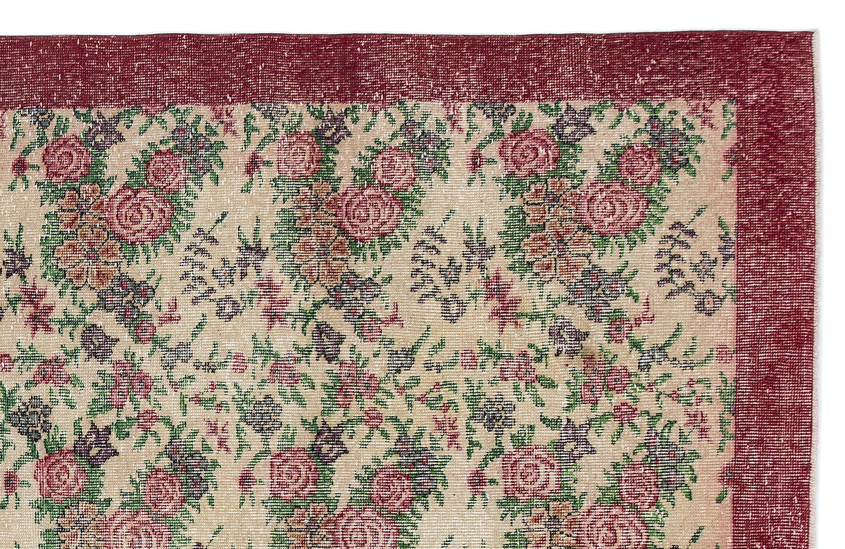 Distressed beige rug with a floral pattern in red, green, and purple, featuring a wide solid red border.