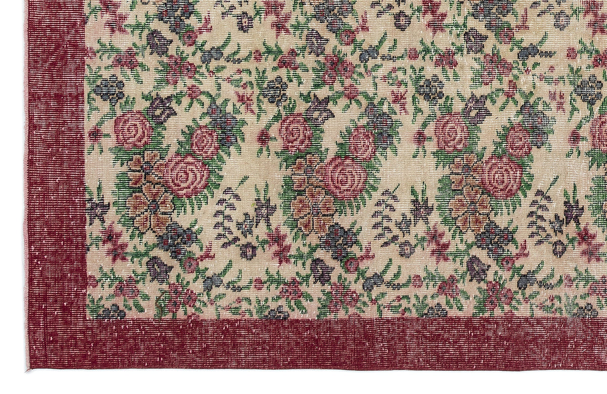 Beige rug with a floral pattern in red, green, and purple, featuring a solid red border.