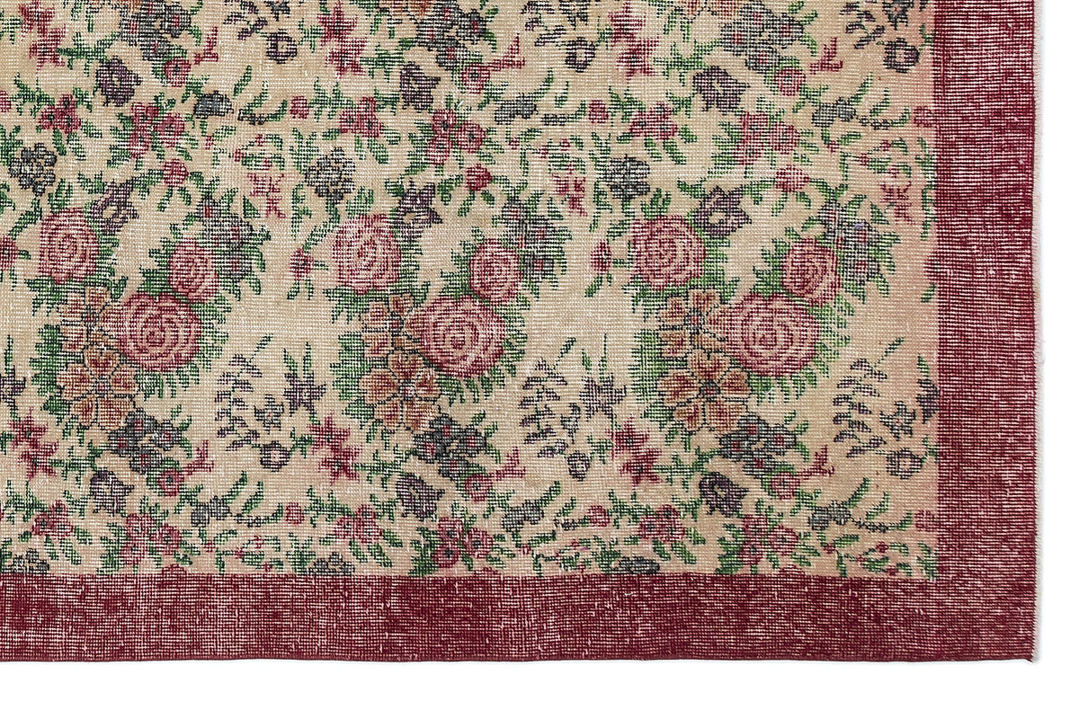 Beige rug with a floral pattern in red, green, and dark grey, featuring a solid red border.