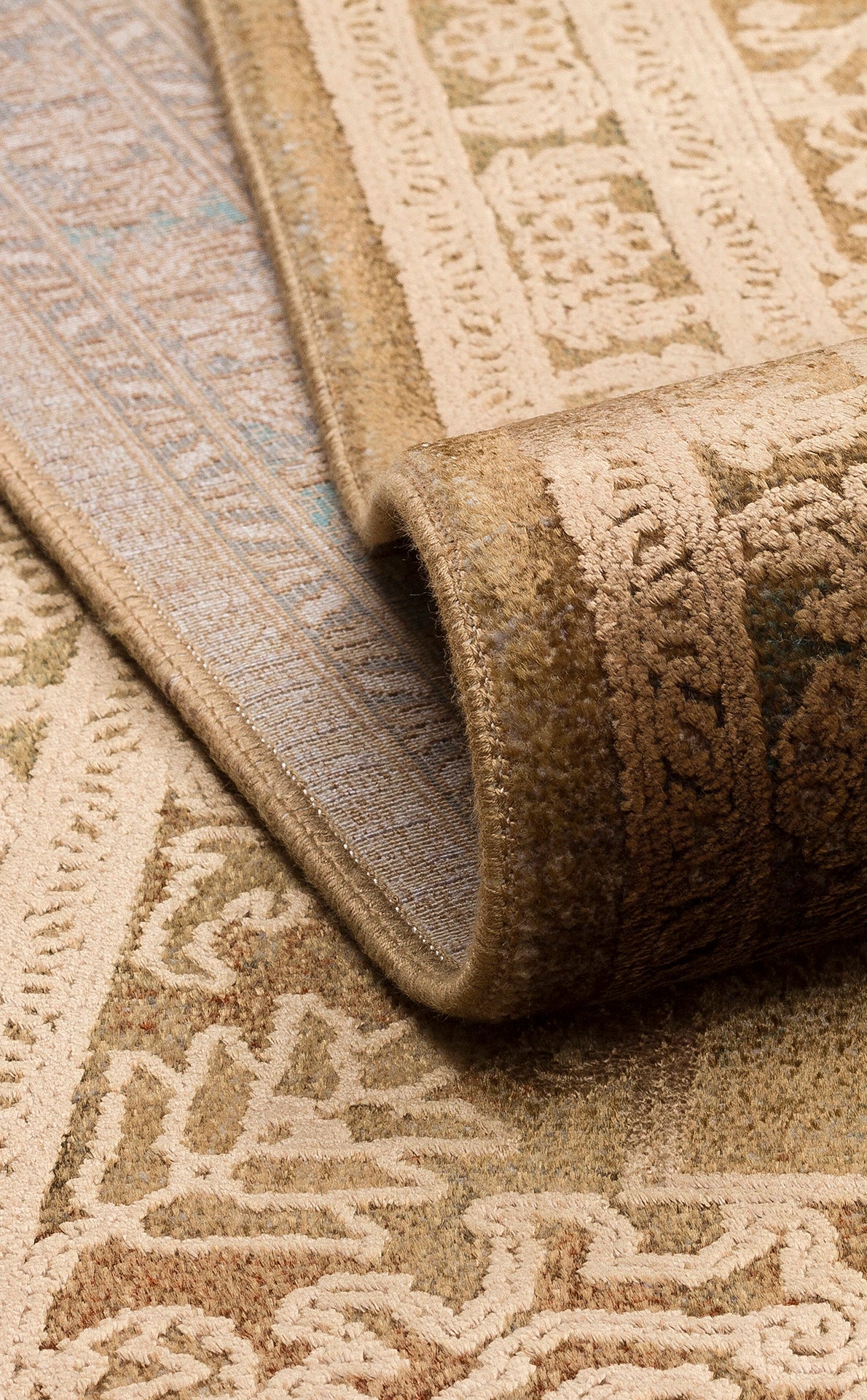 Folded tan and beige rug featuring a traditional ornate floral pattern with a visible woven edge.