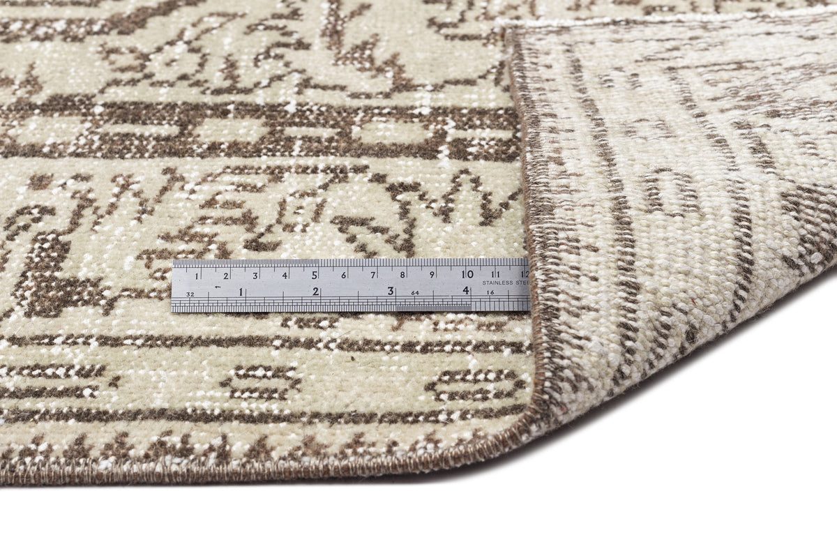 Beige and brown rug with a distressed traditional pattern, shown with a metal ruler for scale on a white background.