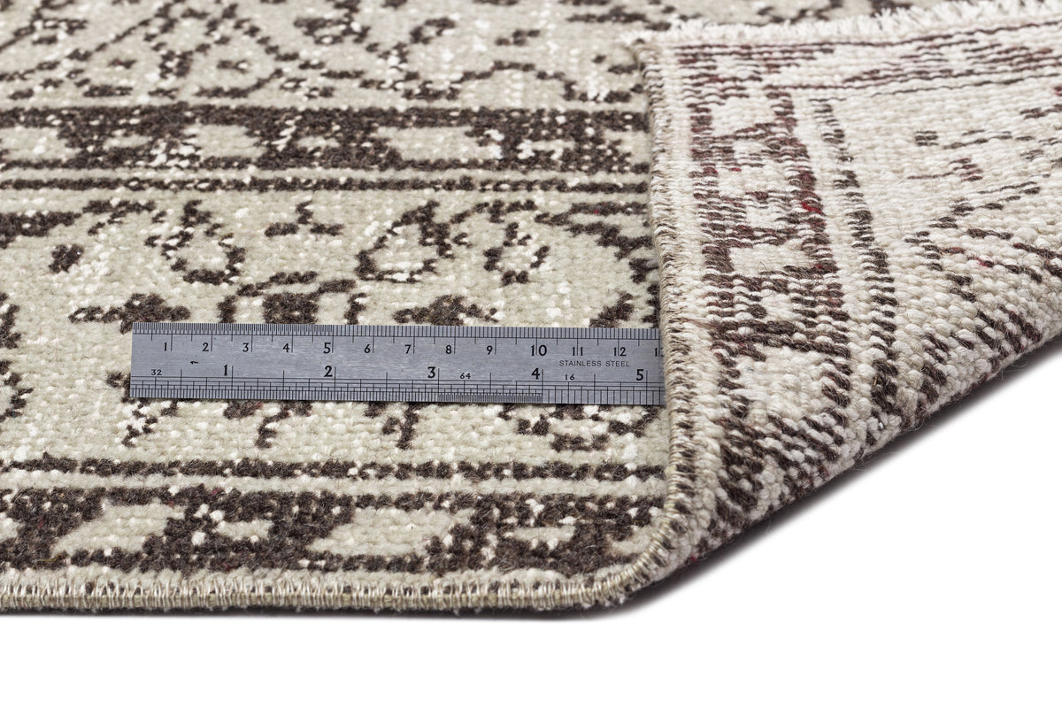 Beige and dark brown rug with a distressed traditional pattern, shown folded with a metal ruler for scale.