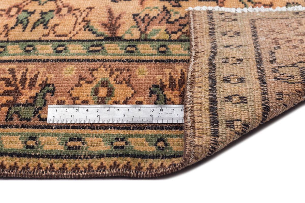 Tan and green traditional rug with a floral border and geometric pattern, shown with a metal ruler for scale.