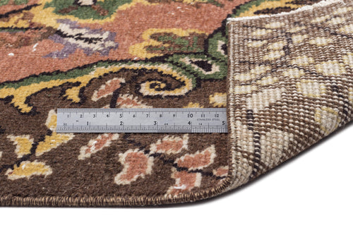Load image 1 in gallery view. Floral patterned rug in brown, green, and yellow with a folded corner showing the woven backing and a metal ruler.